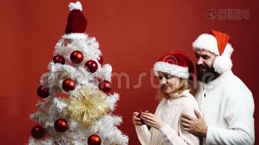 可爱的一对幸福的夫妇在圣诞树旁迎接新年。 一对年轻夫妇戴着新年`帽子装饰圣诞节视频
