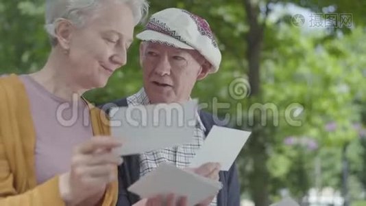 特写肖像可爱的成年夫妇看着老照片，回忆着坐在公园长凳上的快乐时刻视频