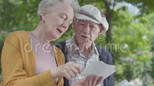特写肖像可爱的成年夫妇看着老照片，回忆着坐在公园长凳上的快乐时刻视频