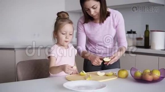 妈妈和女儿在家做健康的食物，玩得开心。 年轻女子在面前的桌子上切黄苹果视频