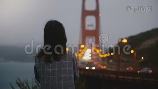 后景年轻放松的女人看标志性的金门大桥，在黑暗的夜晚，大风的交通景观。视频