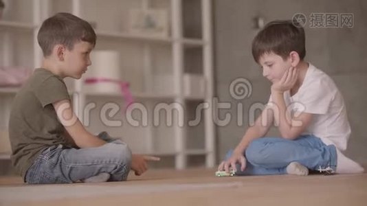 两个可爱的兄弟坐在地板上玩玩具车坐在地板上在家里。 小兄弟花时间视频