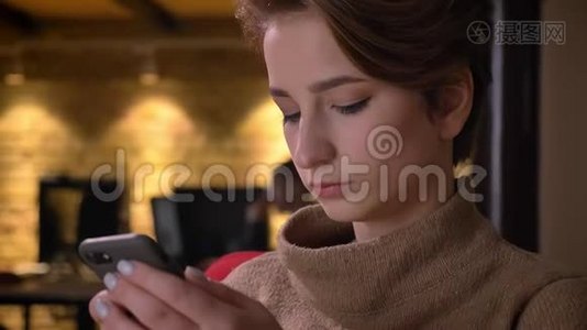 一位短发年轻女性的特写肖像，在办公室里专注地看着智能手机。视频