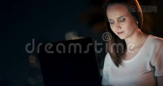 年轻女子夏夜坐在草地上，手提电脑在城里视频