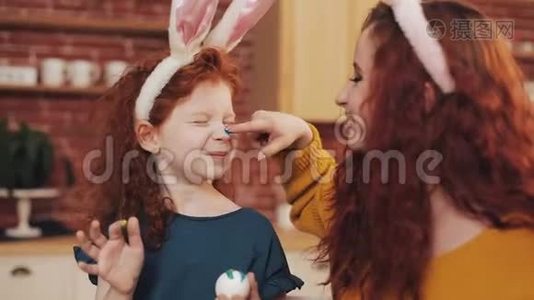 复活节快乐。 年轻的母亲和她的小女儿互相画`鸡蛋和脸。 家庭笑话视频