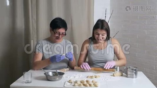 一个怀孕的女孩和她的母亲坐在家里厨房的一张桌子旁，午餐准备饺子和肉末，卷起来视频
