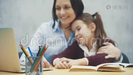 妈妈和女儿拥抱着自己，看着桌子上的一台灰色笔记本电脑。 在这模糊的背景下。 的概念视频