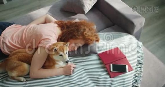 迷人的年轻女子睡在沙发上，拥抱可爱的石巴狗视频