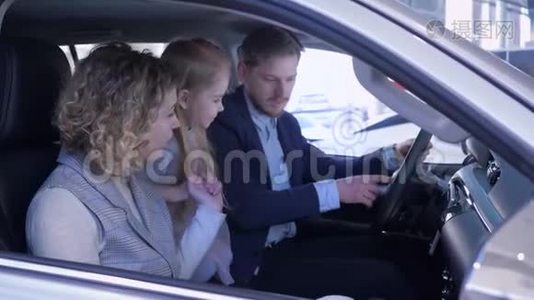 家庭在汽车经销商，幸福的夫妻和孩子考虑新汽车，而坐在机舱在汽车。视频