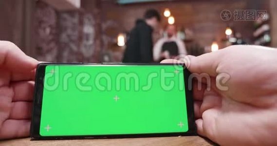 在一家繁忙的餐馆、咖啡店或酒吧里，男人在绿色屏幕上刷卡视频