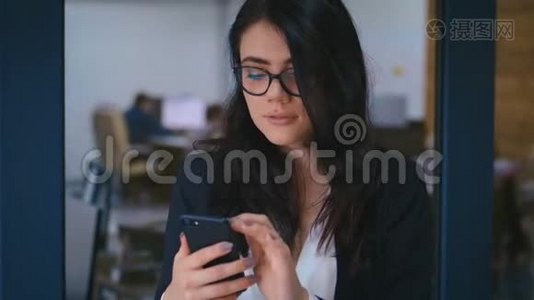 办公室使用智能手机的美丽年轻女性肖像。 商务女士正式着装时的打字信息视频