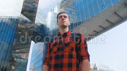 穿着格子衬衫，背着背包环顾城市的旅游者。大玻璃城市建筑背景。视频