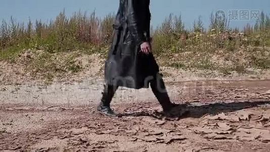 一个穿着黑色雨衣和帽子的硬汉穿过沙漠。 他看起来像个追踪者。视频