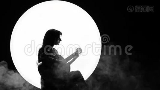 女音乐家的剪影。 一个年轻的女人坐在白色圆圈背景上弹着一把吉他，就像满月一样视频