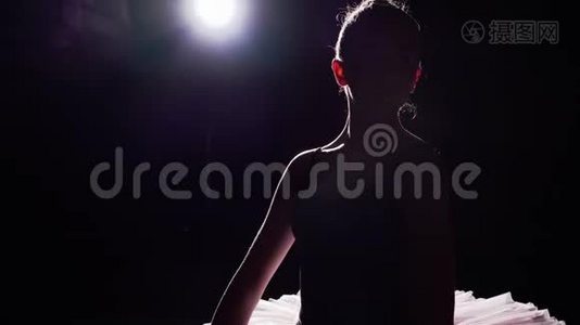 漂亮的年轻芭蕾舞演员站在她的尖角芭蕾舞鞋上，聚光灯下的黑色背景在演播室。 女孩表演视频