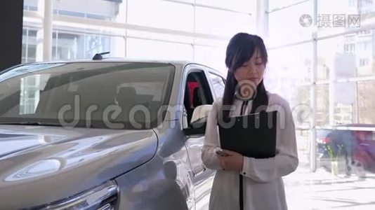 在汽车中心的新车旁，微笑的女经理竖起了大拇指视频
