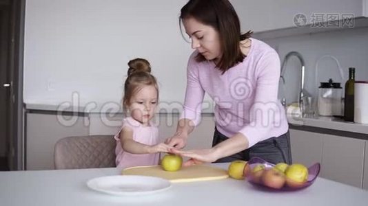 妈妈和女儿在家做健康的食物，玩得开心。 年轻女子在面前的桌子上切黄苹果视频