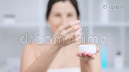 女人用罐子做白色奶油粉底，并展示奶油或面膜视频