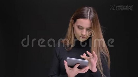 年轻的金发金发女郎专心地看着平板电脑，并把它的绿色屏幕显示成黑色相机视频