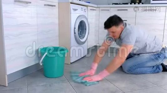 穿着橡胶手套的不高兴的疲惫的男人在厨房里洗和用力地摩擦地板。 侧视。视频