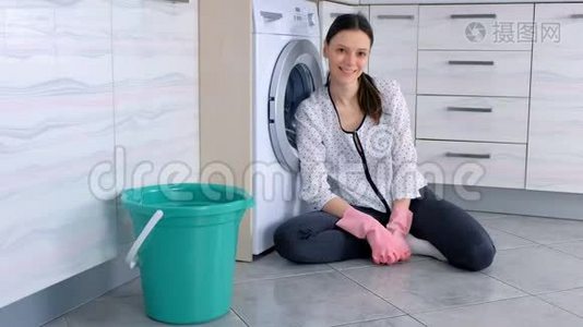 幸福的女人在厨房地板上戴着粉红色的橡胶手套，清洁后看着相机。视频