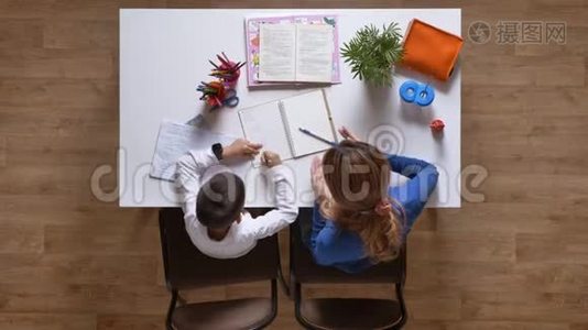 年轻的母亲帮儿子学习，小男孩从笔记本上擦掉一些东西，坐在桌子后面，孩子在做视频