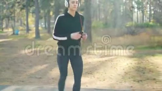 多莉拍摄的可爱的黑发女孩在公园慢跑和听收音机耳机独自练习。 现代技术视频