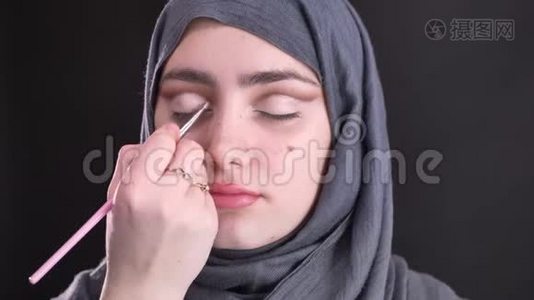 在黑色背景下，女性双手用薄薄的画笔为美丽的穆斯林妇女做眼妆的肖像。视频