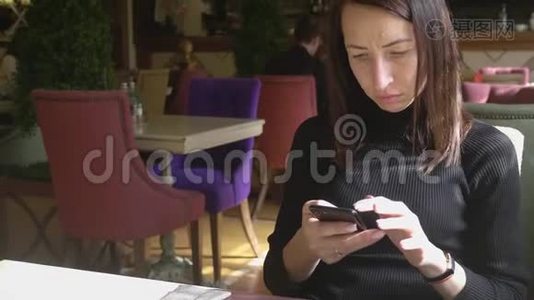 年轻的馄饨在工作休息的时候坐在舒适的咖啡店里，一边用手机，一边迷人的快乐女性阅读视频