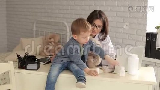 一位年轻的女医生在一家儿童诊所`办公室里和一个小男孩玩耍。视频