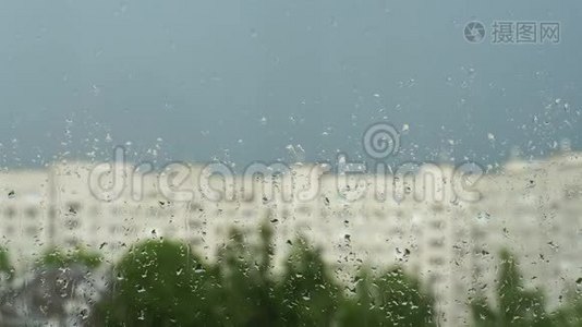 窗户玻璃上的水滴。 城市里的夏雨，蓝天，模糊的房屋轮廓和绿树。 4K视频视频