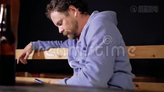 一个留着胡子和胡子的人正坐在桌旁用手机写短信，面前的桌上放着两瓶视频