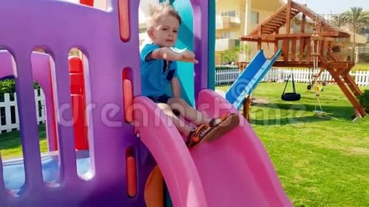 在公园儿童游乐场里，一个快乐微笑的幼儿男孩骑在滑梯上视频