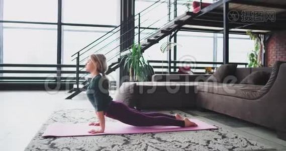 在客厅阁楼的垫子上，有魅力的女人在家里伸展身体练习瑜伽视频