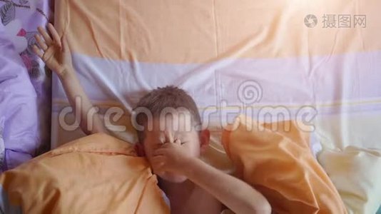 一个小男孩在床上打哈欠和伸展的俯视图视频