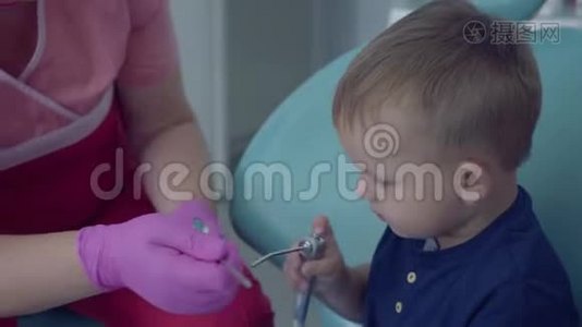 牙医准备检查坐在牙科办公室椅子上的无忧无虑的小男孩的牙齿。 女性专业人员视频