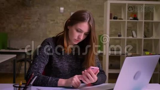 年轻的白种人红头发的女人在智能手机上冲浪，并改变了情绪从喜悦到困惑在办公室。视频