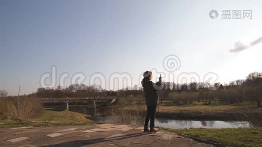 年轻女子在波罗的海国家城市萨比莱的背景下，用她的手机应用程序“河流”拍照视频