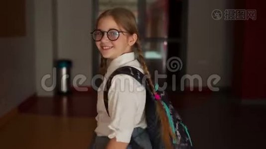 戴眼镜的小女孩带着书包在学校走廊的背景上。 回到学校视频