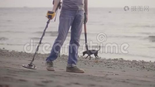 无法辨认的人带着电子金属探测器在海滩上用金属探测器扫描沙子，发现贵重物品。视频
