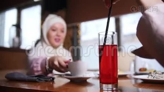 一位年轻的穆斯林妇女坐在现代咖啡馆里交谈。 一个女人用吸管搅拌饮料视频