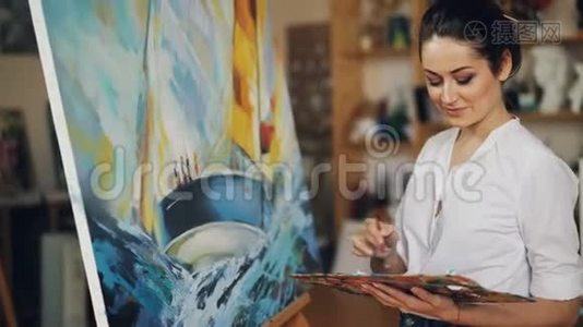 微笑的年轻女子正在油画颜料中的画布上画着一幅画，描绘着船和蓝色的海浪视频