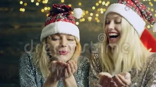 两个女孩戴着`顶帽子，把他们的手掌上的雪吹掉了。 新年`心情。 庆祝新年的概念。 二.视频