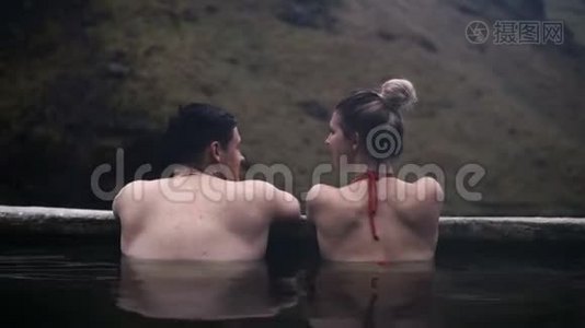 冰岛温泉中年轻夫妇的后景。 旅行的男人和女人在山区山谷放松。视频