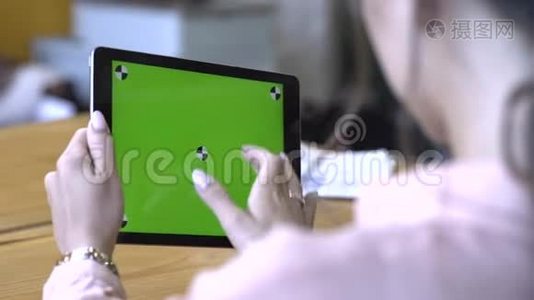 一位棕色头发的年轻女士坐在桌子旁，在彩色钥匙绿色屏幕上滑动着她的平板电脑视频