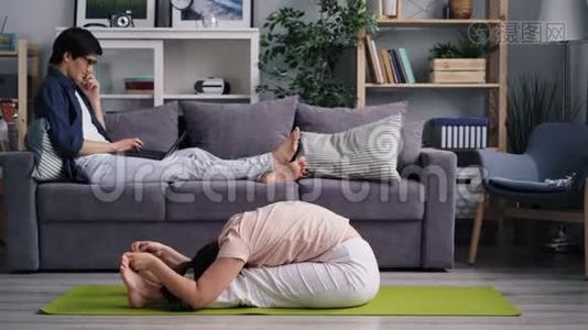 女朋友在男朋友用手提电脑在手机上聊天时做瑜伽视频