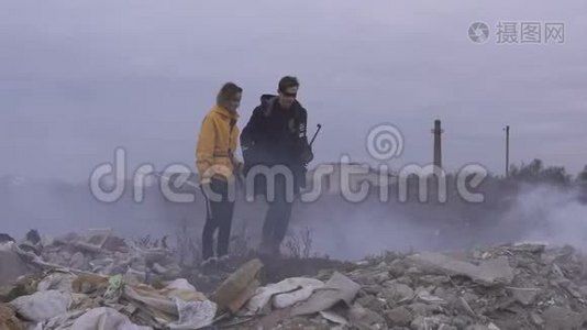 帮助女孩在垃圾堆之间跳跃的家伙。几个拿着武器的幸存者被烟雾笼罩视频