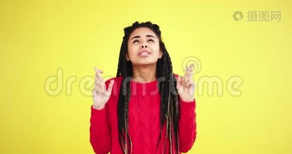 在一个有着黄色背景的工作室里，一位富有魅力的、风趣幽默的非洲多民族女士，一位交叉着手指和恐惧的人视频