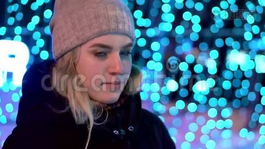 一个年轻迷人的女孩戴着帽子，在冬天的外面站在蓝色的灯光背景上。 圣诞节和新年视频