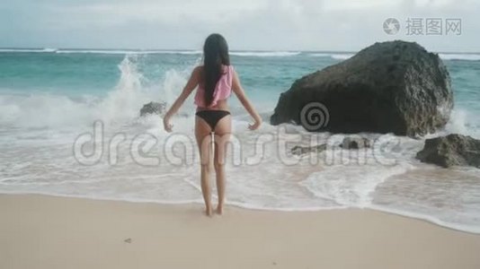 穿着泳装、双臂张开的苗条女孩站在海滩上，看着海浪，稳重视频